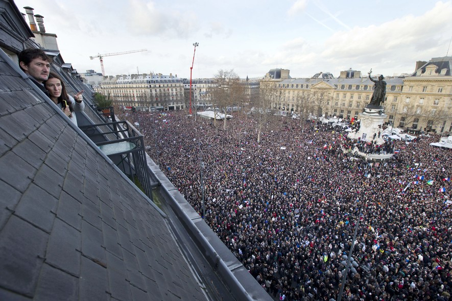 Pessoas assistem, de cobertura na Praça da República, em Paris, ao encontro de milhares de pessoas para se manifestar pela liberdade de expressão e em solidariedade às 17 vítimas do ataques terroristas da semana passada na França