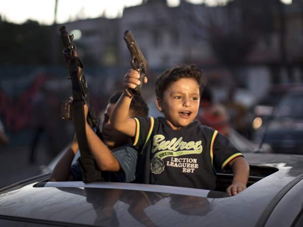 Crianças segurando armas participam das comemorações pelo acordo de cessar-fogo duradouro nesta terça (26) na cidade de Gaza (Foto: AFP PHOTO/MAHMUD HAMS)