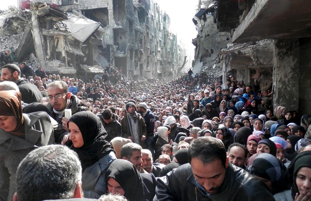 Palestinos vivendo em um campo de refugiados em Damasco, Síria, fazem fila para receber alimento. Segundo a ONU, eles estão vivendo a base de ração animal devido a falta de suprimento por causa da gurra civil na Síria (Foto: AP Photo/UNRWA)