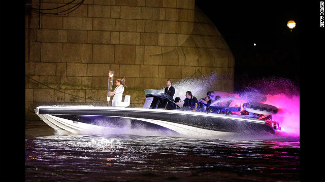 David Beckham passa sob a Tower Bridge dirigindo um barco chamado "Max Power", que carrega a Tocha Olímpica.