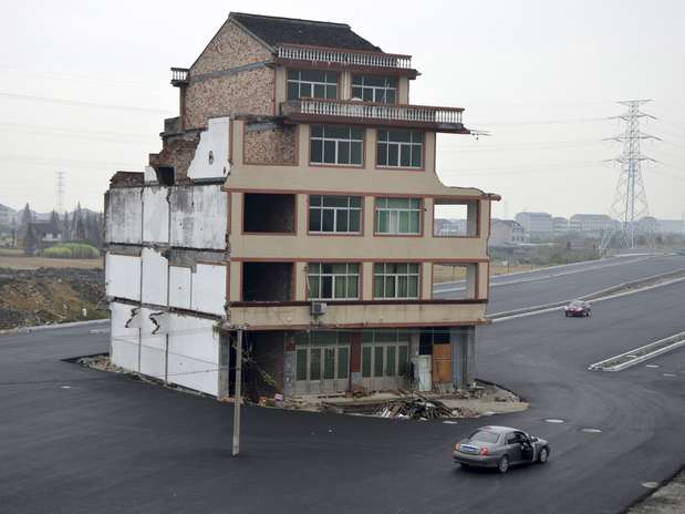 Carro passa ao lado de casa solitária em meio à rodovia recém-construída em Wenling, na província de Zheijang. Um casal de idosos se recusou a assinar um acordo em que receberia uma indenização em troca da demolição da residência. Segundo a Reuters, eles dizem que a compensação oferecida não cobria os custos para erguer uma nova casa. Com isso, a estrada foi construída ao redor da moradia  Foto: Reuters