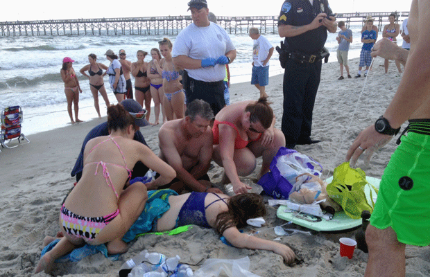 Equipes de emergência ajudam uma das vítimas do ataque de tubarão em Oak Island, no domingo (14) (Foto: AP)