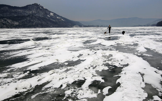 Homem anda com seus cachorros em trecho congelado do rio Danúbio neste sábado (11), em Nagymaros, na Hungria (Foto: Laszlo Balogh / Reuters)